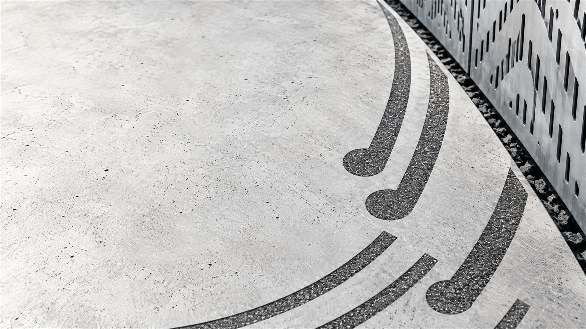 Cast concrete surface with dark aggregate inlay lines meeting a perforated steel edge